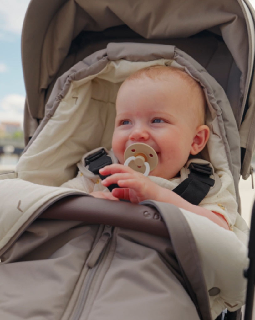 Vauva rattaissa, tuttia suussa, taustalla sininen taivas.