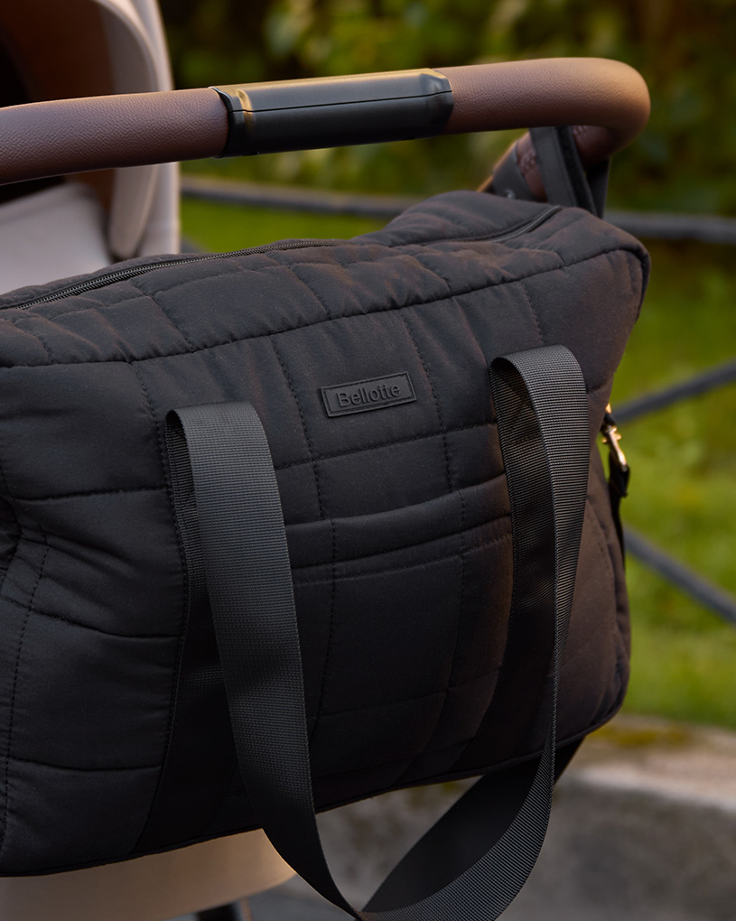 Mustavillainen hoitolaukku vaunujen kahvassa ulkona.