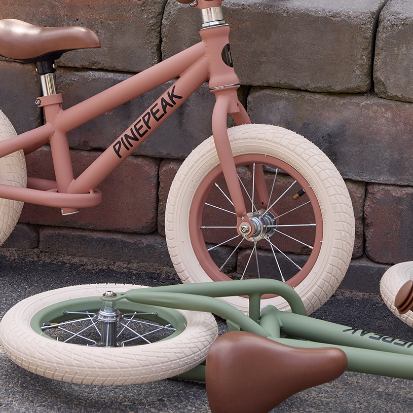 Keltainen lastenpyörä, jossa kori, apupyörät tyynyjen ja seinän edessä.