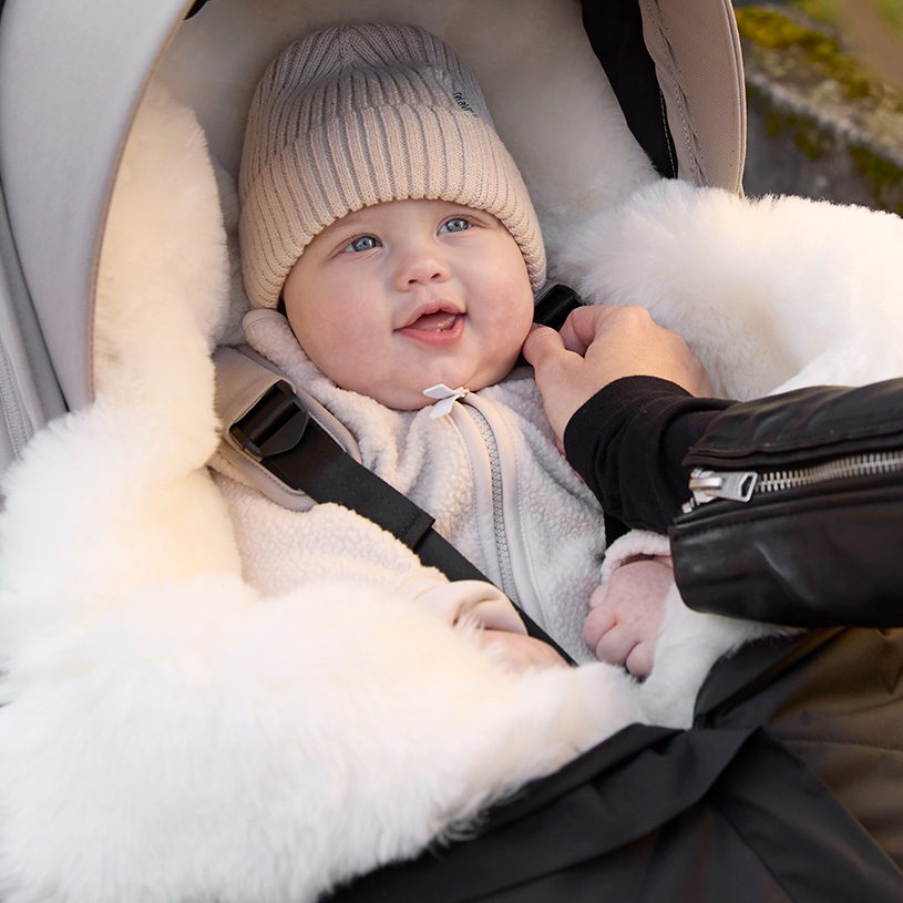 Vauva tutilla nukkuu mustassa haalarissa turvaistuimessa.