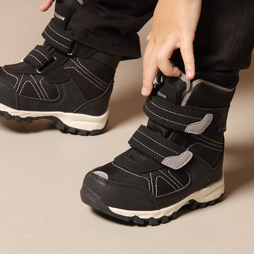 Lapsen käsi pukemassa beigeä tarranauhakenkää.