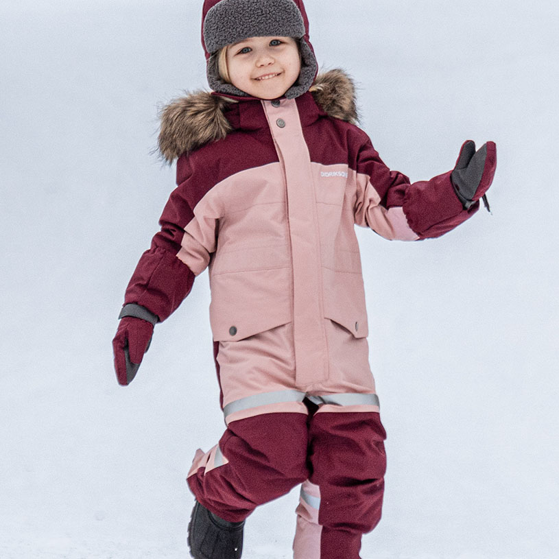 Lapsi talvihaalarissa ja hatussa leikkii lumessa.