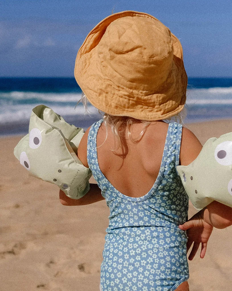 Lapsi uimapuvussa ja aurinkohatussa rannalla kellukkeilla.