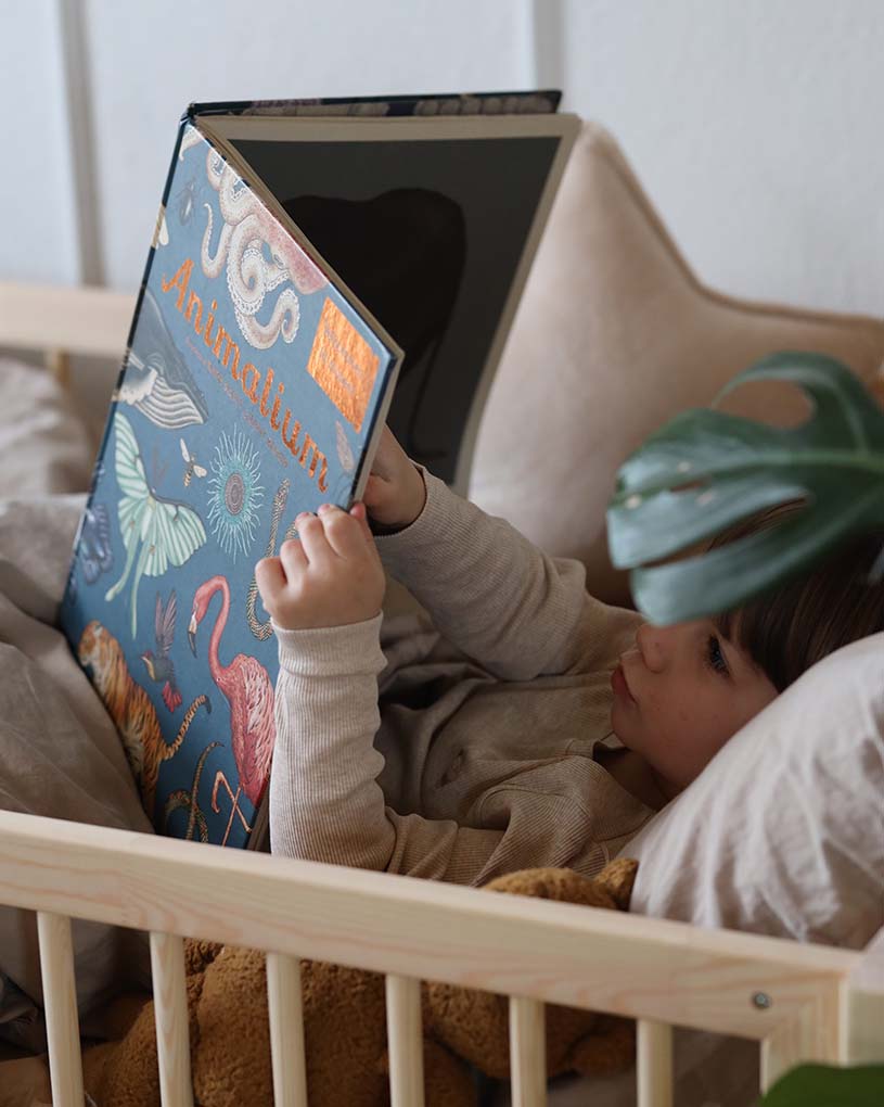 Lapsi sängyssä lukee isoa kirjaa eläimistä.