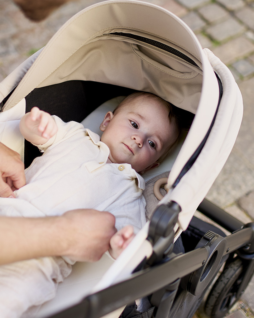 Mustat lastenvaunut, joissa hopeinen runko ja ruskea kahva, lattiapinnan päällä.