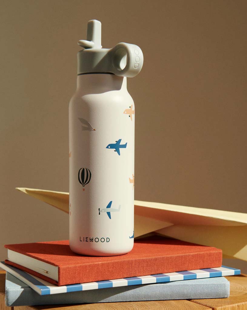 Valkoinen vesipullo lentokonekuviolla kirjojen ja paperin päällä.