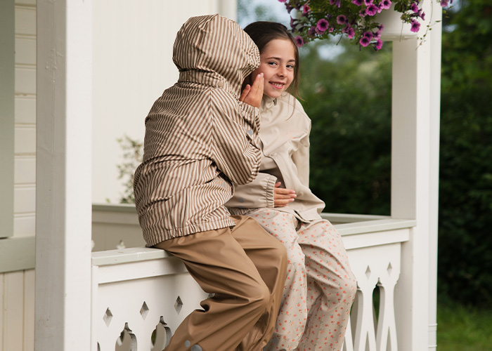 Kaksi lasta istuu parvekkeella ja kuiskaavat toisilleen, tekstinä 'Kenza X Viking'.