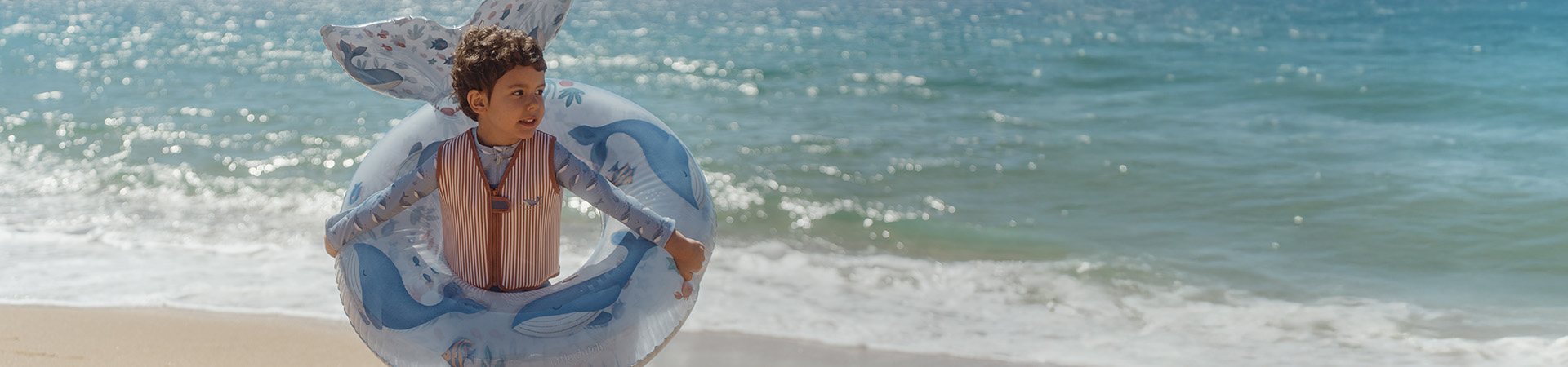 Lapsi rannalla uimarenkaan kanssa, meri taustalla. Teksti: "Uutta kauteen".