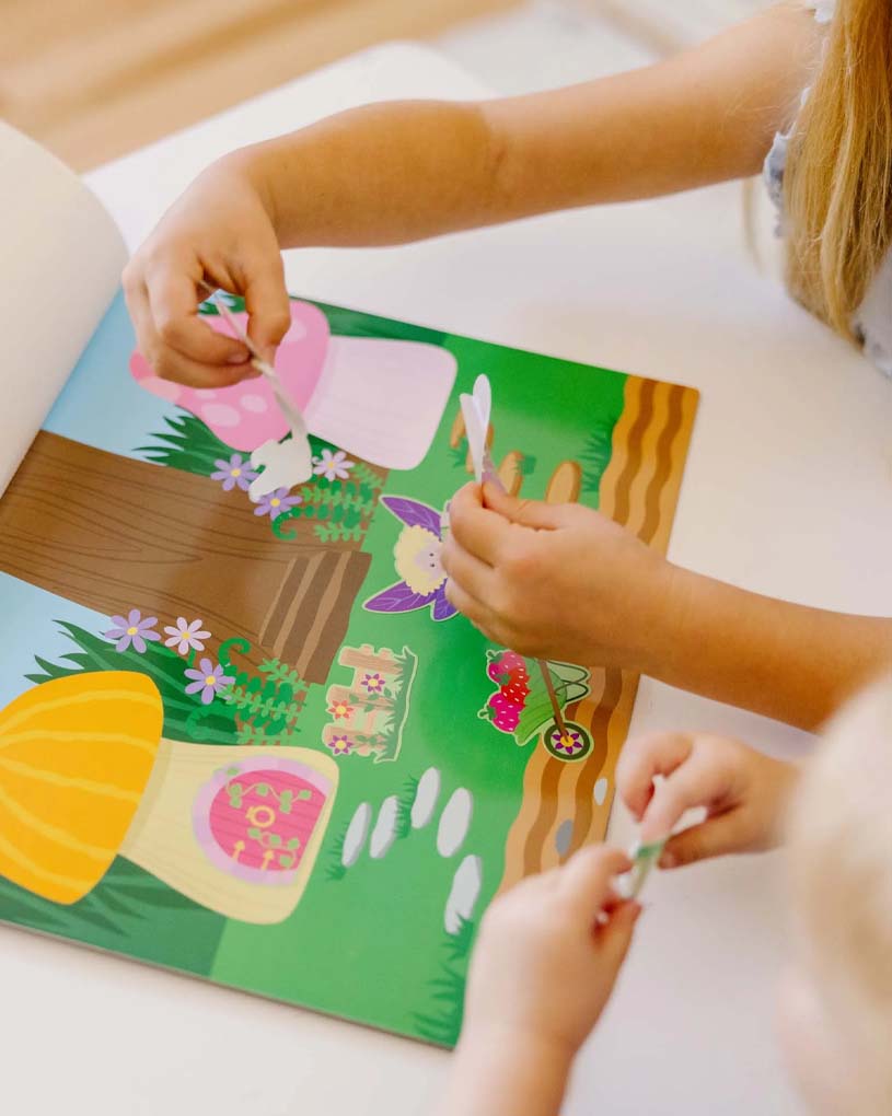 Kaksi lasta leikkii tarrailla värikkäässä satukirjassa.