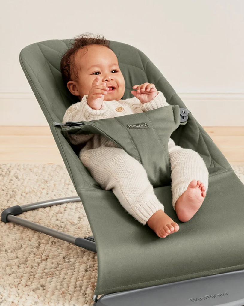 Vauva harmaassa tuolissa, hymyilee ja nostaa kädet ylös.