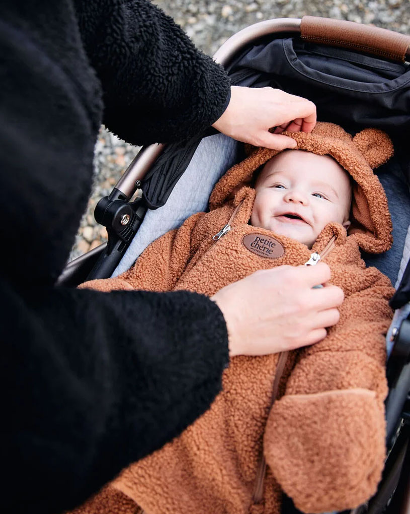 Vauva ruskeassa nallehaalarissa hymyilee vaunuissa.