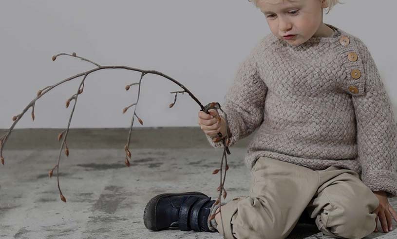 Lapsi harmaassa paidassa ja beigessä housussa leikkii oksalla sisällä.