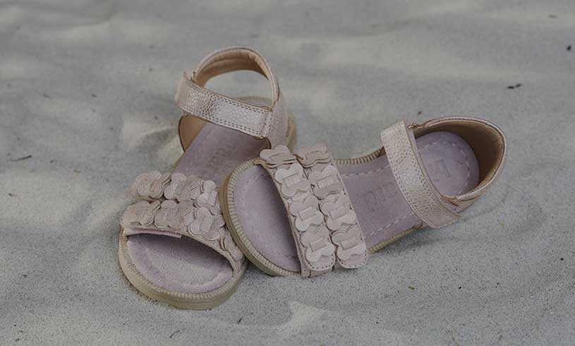 Beiget sandaalit kukkakoristeilla hiekalla.